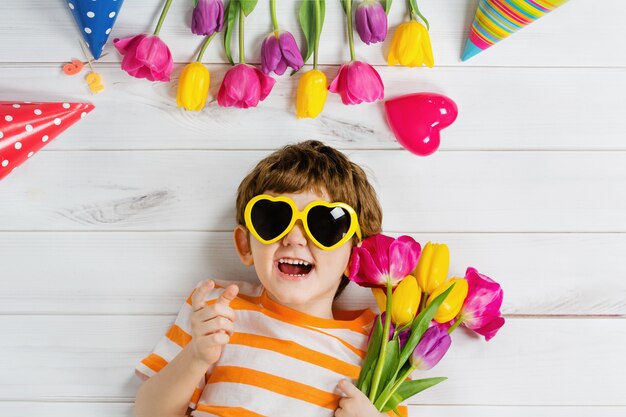 Laughing baby lying on the wooden floor with glasses for heart shape on carnival party