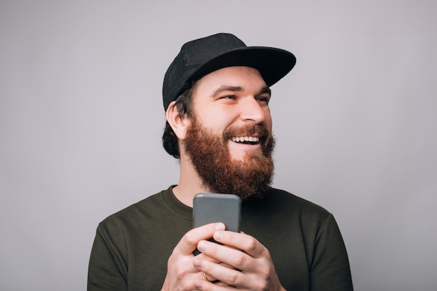 Laughing bearded man is holding his phone looking aside.