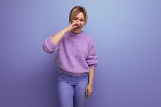 Laughing blond young woman in a lilac sweater on a bright background