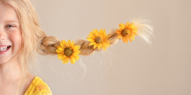 Laughing blonde caucasian girl with yellow daisy flowers in braids which funny stick out to the side Half face close up portrait