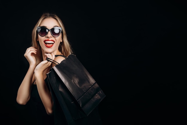 Смеющаяся блондинка демонстрирует бумажный пакет модных покупок
