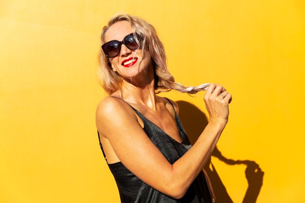 Laughing blonde with long hair wearing sunglasses on yellow