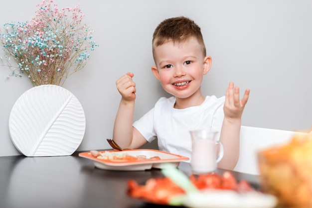 Laughing boy eats delicious pasta at the table in the kitchen