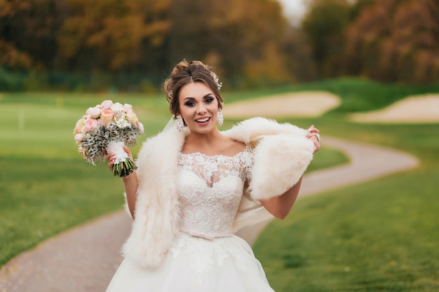 Laughing bride with bouquet in hands on a field of green grass