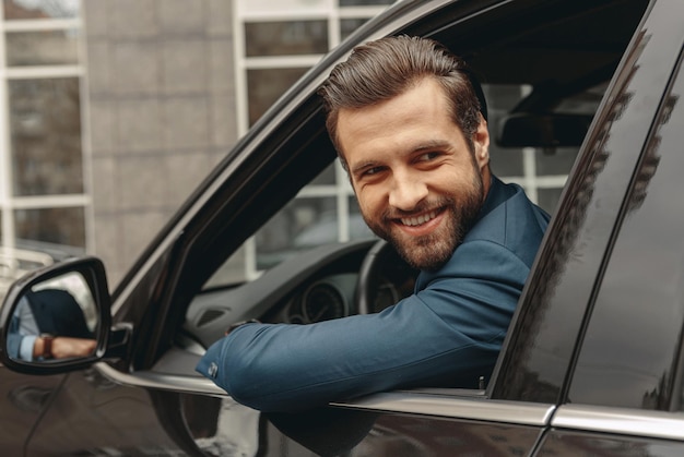 Laughing caucasian business man in suit looking away in salon of automobile