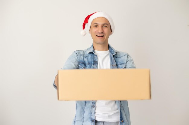 Laughing delivery man in santa claus hat on the phone, standing and holding carton box on one hand. isolated on white.