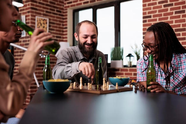 Laughing diverse friends sitting together at home while playing strategy boardgames. Happy confident people sitting at table in living room while enjoying fun leisure activity.