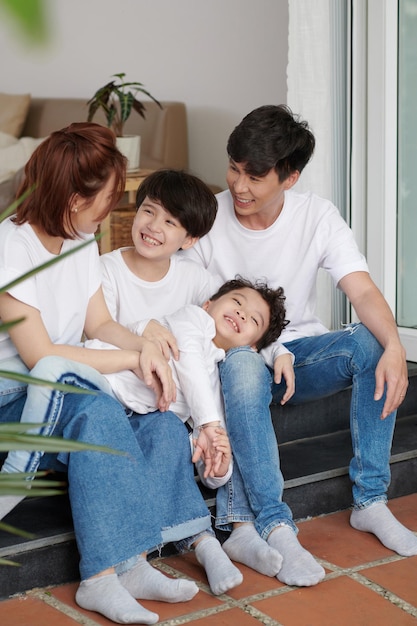 Laughing family of four in jeans and white tshirts sitting on house porch