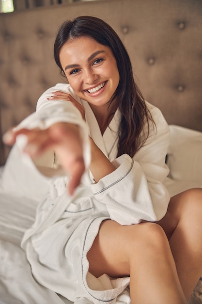 laughing female sitting on the bed while posing and looking at the photo camera