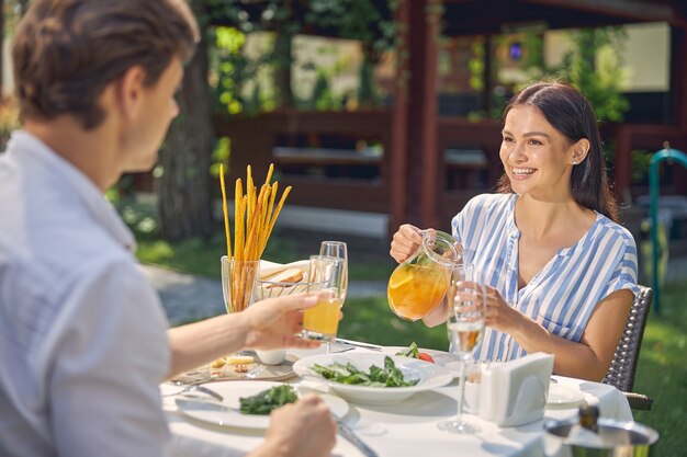 laughing female with orange lemonade in hand while looking to the man at the table in restaurant