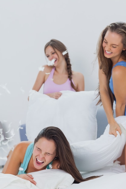 Смеющиеся друзья, играющие на подушках в постели