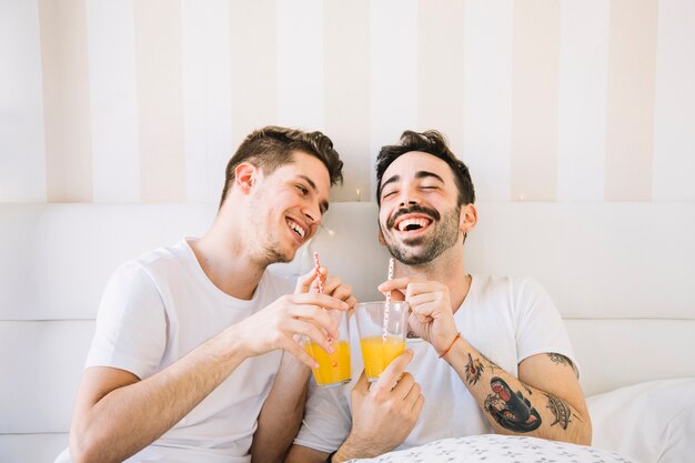 Laughing gay couple having juice in be