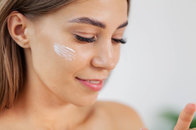 Laughing girl applying moisturizing cream on her face.