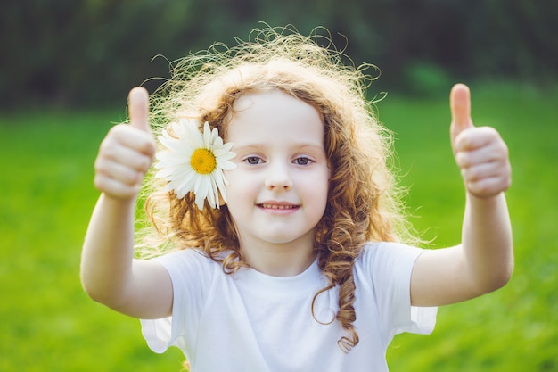 Laughing girl with daisy in her hairs, showing thumbs up.