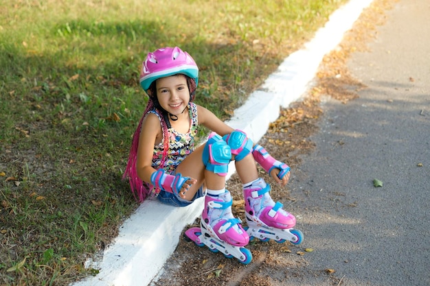 Laughing girl with pigtails in protective helmet and roller skates sat down to rest after training