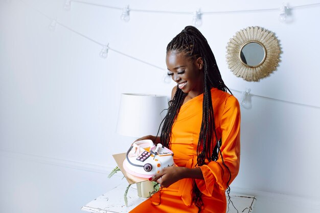 Photo laughing grateful fortunate african american woman in orange dress hold cake in shape of medicine ch