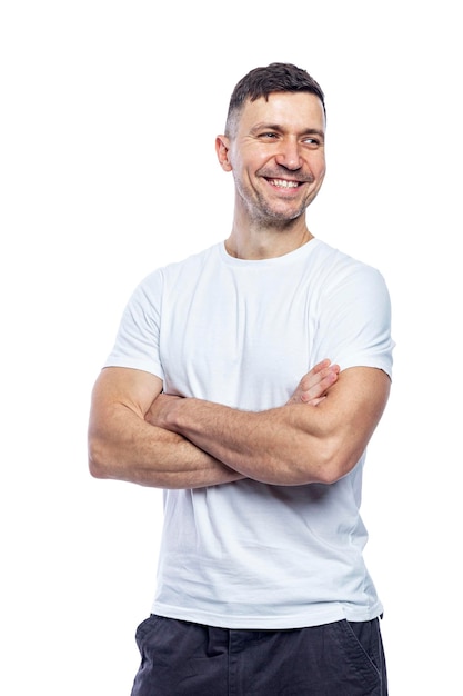 Laughing handsome man in a white tshirt stands with crossed arms and looks away Positive attitude and professionalism Isolated on white background Vertical