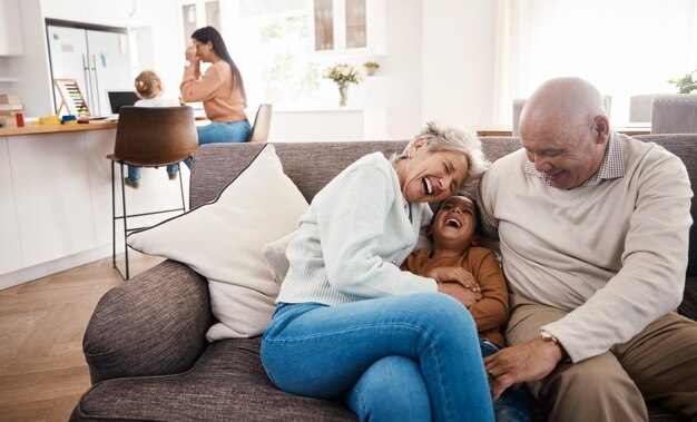 写真 幸せに笑い、子供を子守する祖父母がソファで絆を深め、面白いことをする笑顔の漫画と少年がリビングルームのソファで年配の男性と女性に話し、充実した時間を過ごします