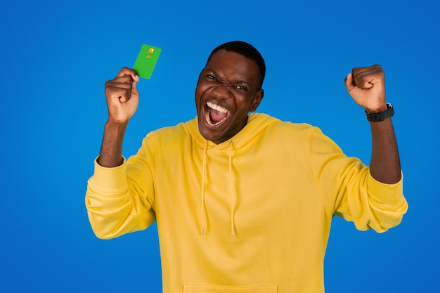 Laughing happy excited young black guy shows credit card rejoices victory celebrates success