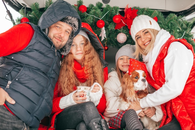 Laughing happy family playing with small puppy dog King Charles Spaniel sitting in decorated Christmas car celebrates Christmas and New Year. Happy moments couple with two children.