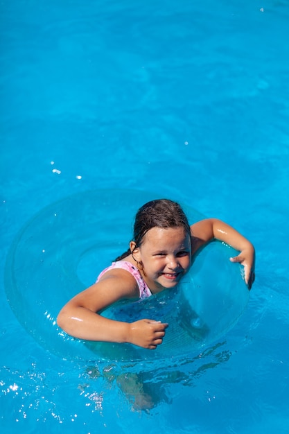 Laughing happy girl learns to swim on a transparent blue inflatable circle in a swimming pool the co...