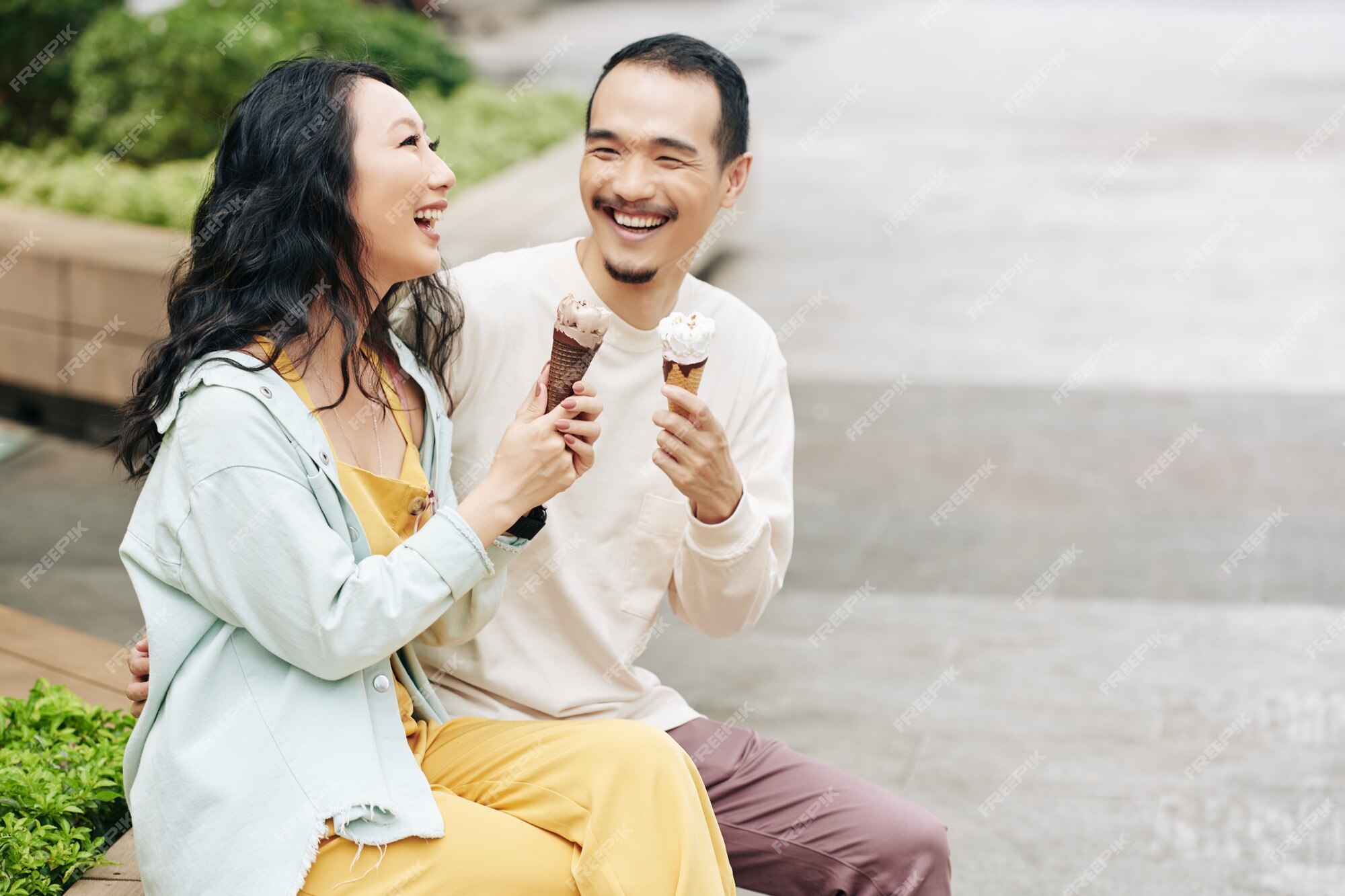 Premium Photo | Laughing happy young asian couple sitting on bench, talking and eating icecreams