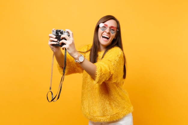 밝은 노란색 배경에 격리된 복고풍 빈티지 사진 카메라로 셀카를 찍는 하트 안경을 쓴 즐거운 젊은 여성이 웃고 있습니다. 사람들은 진심 어린 감정, 라이프 스타일 개념입니다. 광고 영역입니다.