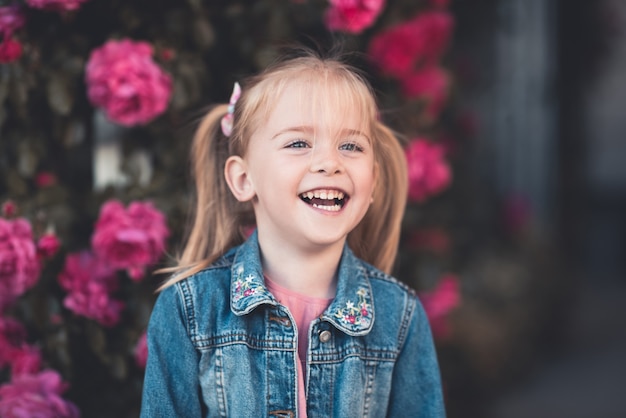 Photo laughing kid girl wearing denim jacket posing over roses