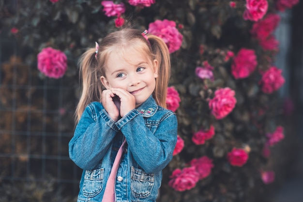 Photo laughing kid girl wearing denim jacket posing over roses