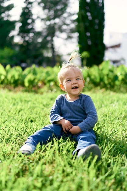 Il bambino che ride con una coda di cavallo si siede su un prato verde