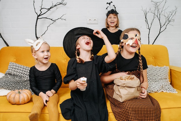 Foto bambini che ridono vestiti per halloween seduti sul divano a guardare cartoni animati divertenti