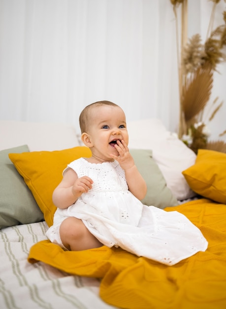 Laughing little girl in a white cotton dress sits on the bed