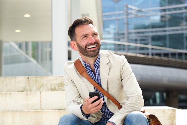 Laughing mature man sitting outdoors with cellphone