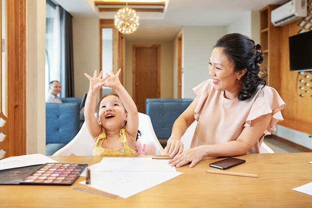 Laughing mother looking at her cute little daughter describing her idea for drawing
