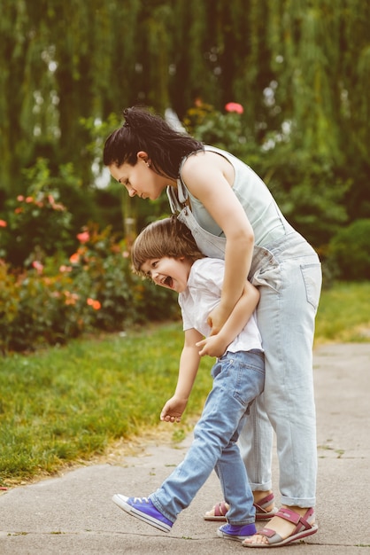 La mamma che ride si rotola sulla schiena del figlio piccolo nel parco