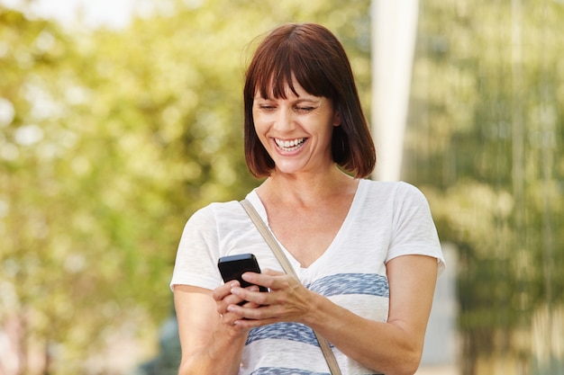 Laughing older woman messaging on smart phone 