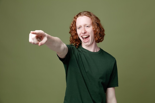 Laughing points at side young handsome guy wearing green t shirt isolated on green background