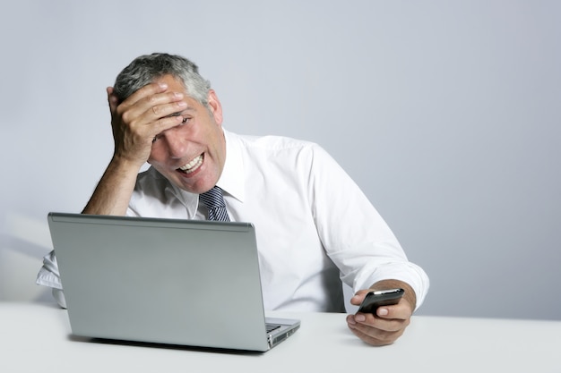 Laughing senior businessman computer phone gesture