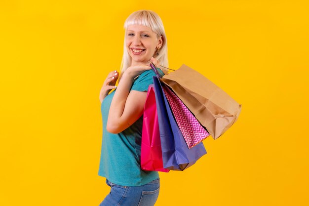 Laughing shopping with bags on sale blonde caucasian girl in studio on yellow background