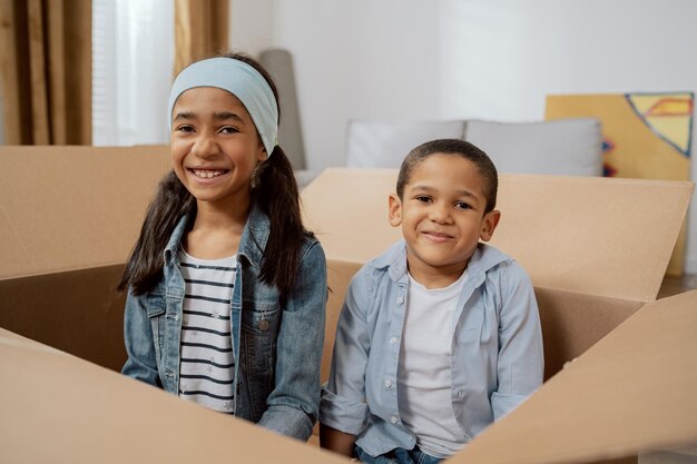 Laughing siblings sit in an empty cardboard box during a move