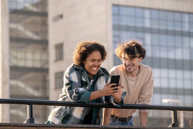 Photo laughing teenage girl with smartphone showing something funny to her boyfriend