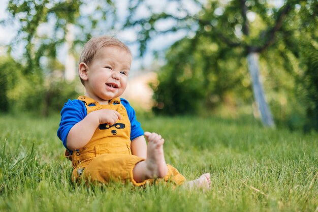 Photo a laughing toddler in fashionable clothes sits on the grass in the garden on a summer day