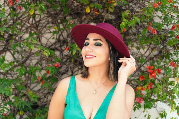 Laughing woman in green dress and red hat, standing in park.