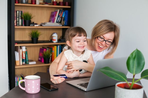 웃는 여자와 그녀의 작은 딸 노트북을보고 온라인 쇼핑