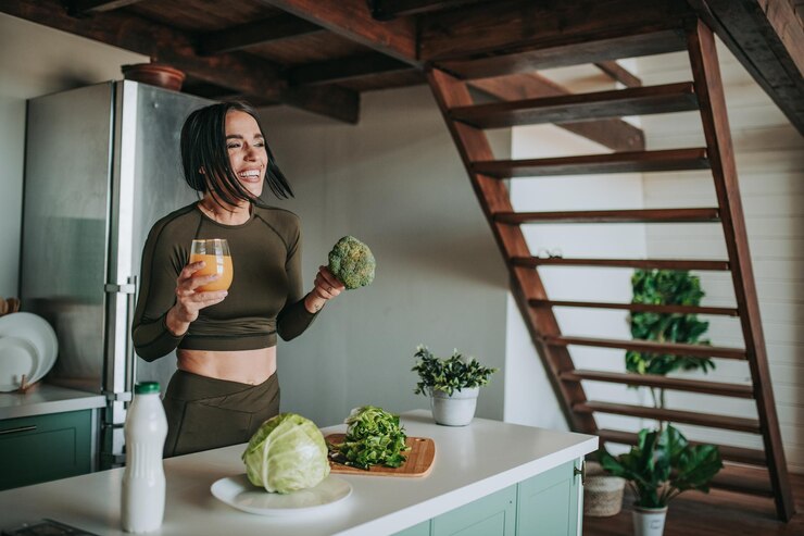 Photo laughing woman holding broccoli while standing at kitchen