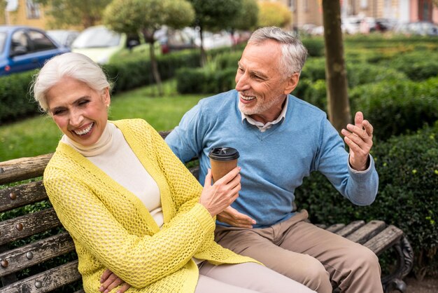 Laughing woman holding coffee cup sitting with husband at park