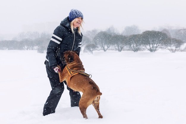 Laughing woman plays with boxer dog in winter park. Love and friendship.