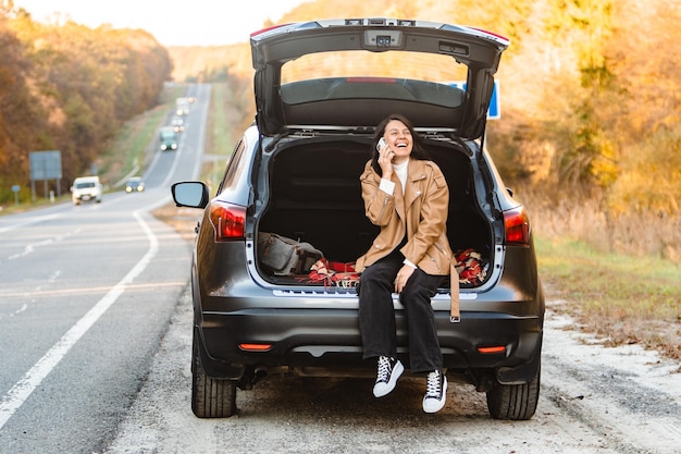 Laughing woman talking on the phone while she sits in the trunk of a car