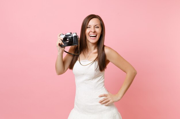 Laughing woman in white dress holding retro vintage photo camera, choosing staff, photographer 