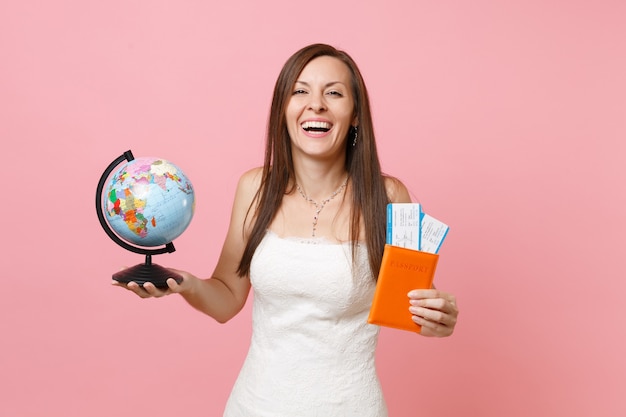 Laughing woman in white dress holding world globe, passport boarding pass ticket going abroad, vacation